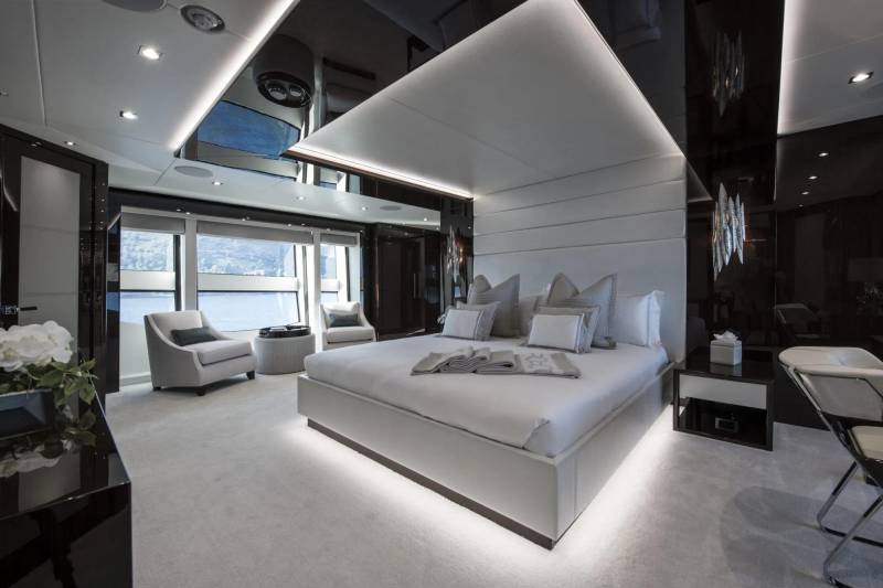 Luxurious yacht bedroom features a king-sized bed, plush seating, and stunning waterfront views through panoramic windows.