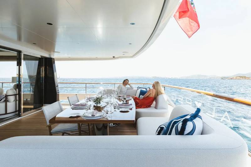 A couple enjoys a leisurely meal on the deck of a luxurious yacht overlooking the sparkling blue sea.