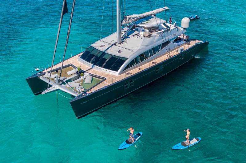 Two paddleboarders enjoy the crystal-clear turquoise waters near a luxurious catamaran.