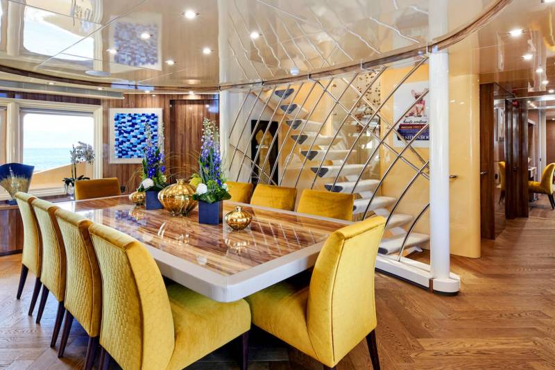 Luxurious yellow chairs surround a polished dining table set with golden vases and floral arrangements on a yacht.
