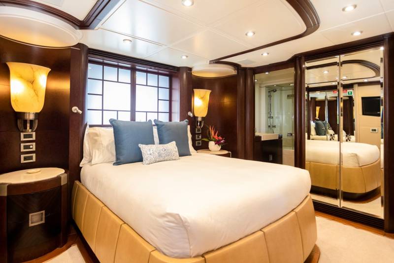 Luxurious yacht accommodations feature a plush bed, elegant lighting, and mirrored closets for a spacious feel.