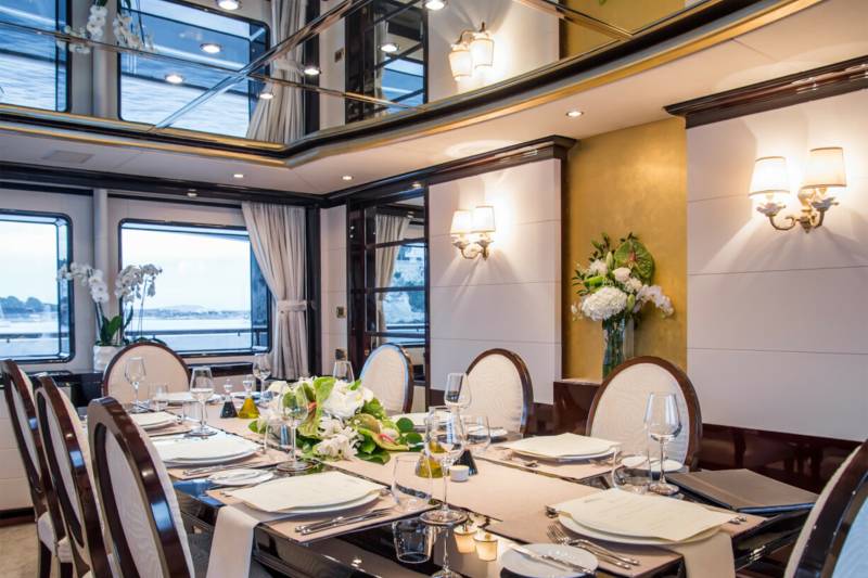 Elegant dining aboard a luxury yacht features a beautifully set table with floral arrangements and scenic ocean views.