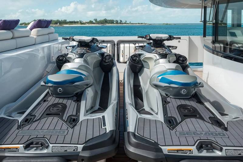 Two sleek jet skis await adventure on the deck of a luxury yacht, poised against a backdrop of turquoise waters and a distant island.