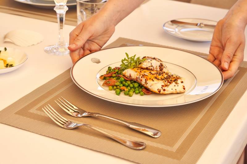 A beautifully presented dish of fish with peas and bacon is served on a white plate with a seashell motif.