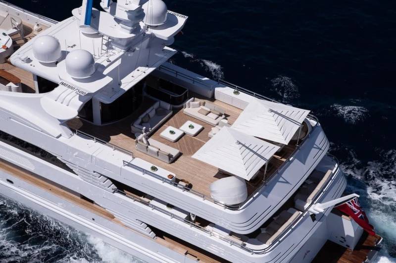 A luxurious white yacht cruises through deep blue waters, its deck adorned with elegant seating and white umbrellas.