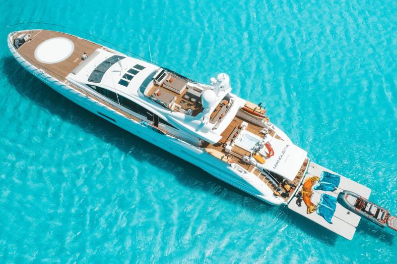 A luxurious white yacht glides through crystal-clear turquoise waters, showcasing its expansive deck and tender.