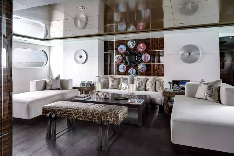 A modern yacht lounge features plush white seating and a striking circular art piece above a dark wood coffee table.