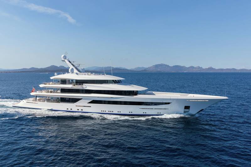 A sleek white superyacht glides through the deep blue ocean under a clear sky with distant mountains.