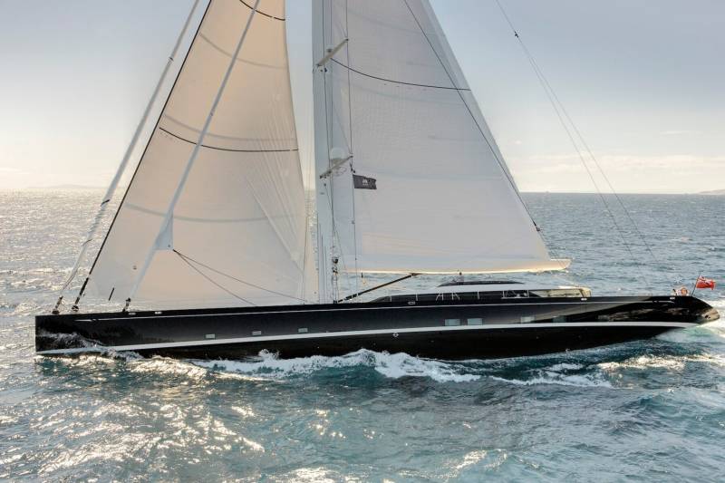A sleek black yacht glides through sparkling blue waters under full sail.