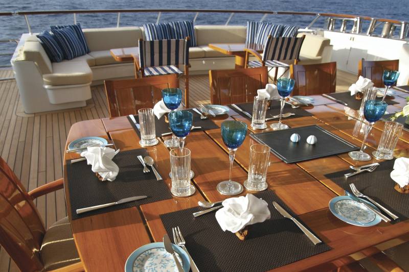A beautifully set dining table awaits guests on the deck of a luxurious yacht, overlooking the ocean.