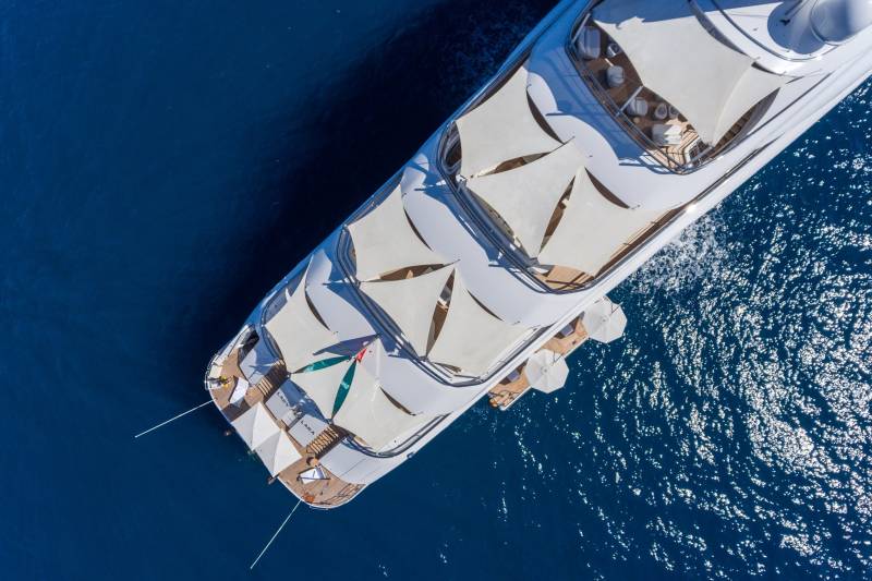 A luxurious yacht glides through the deep blue sea, its white awnings casting intriguing shadows on the deck.
