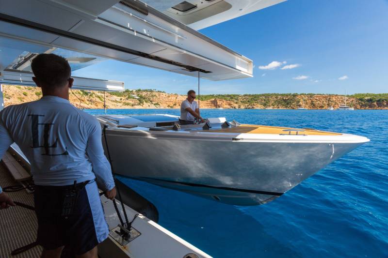 A man steers a sleek yacht through the azure waters of the Mediterranean, with a rugged coastline in the background.