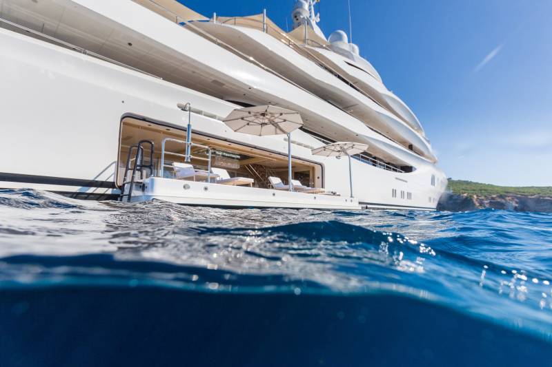 A luxurious white yacht floats serenely on the crystal-clear blue waters under a bright summer sky.