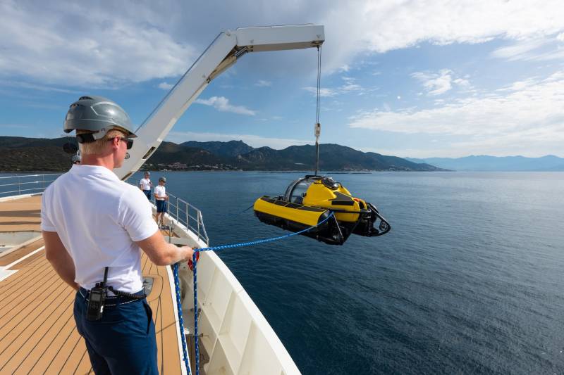 A yellow submersible is carefully lowered into the deep blue sea from the deck of a large ship.