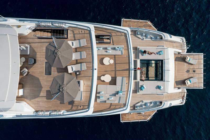 Two women relax on a luxurious yacht deck, one sunbathing and the other reading by a glass-bottom pool.