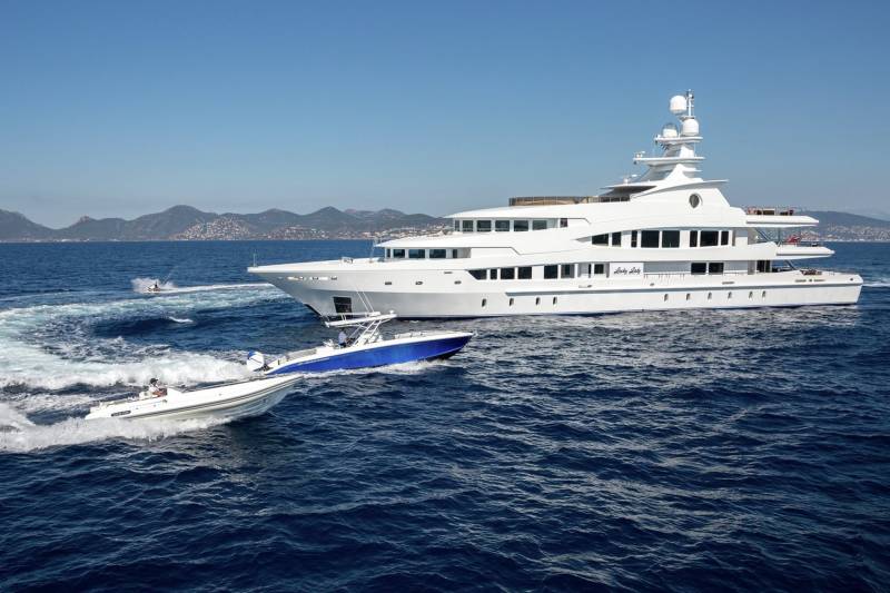 A majestic white yacht cruises through the deep blue sea, accompanied by two smaller speedboats and a jet skier.