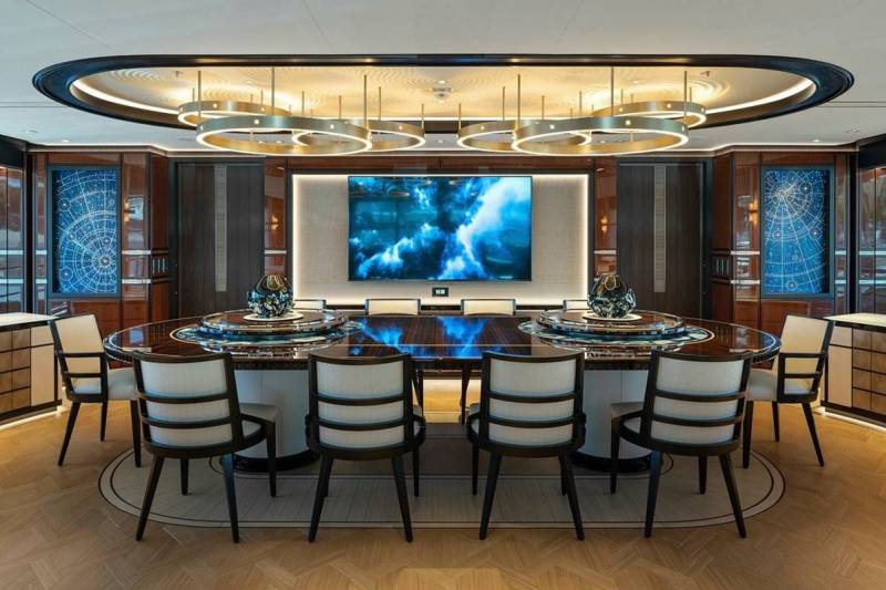 A luxurious oval dining table is set for a formal meal beneath a stunning modern chandelier.