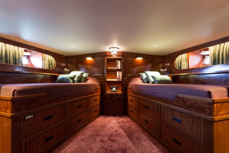 Luxurious twin beds with ample storage are nestled within the richly paneled interior of this elegant yacht cabin.