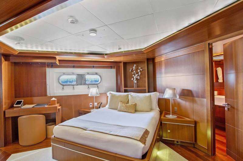 Luxurious yacht cabin features a comfortable bed, elegant wood paneling, and porthole windows offering ocean views.