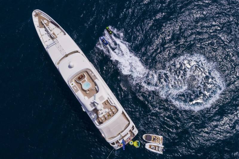 Two jet skis create a swirling wake behind a luxurious yacht anchored in deep blue waters.