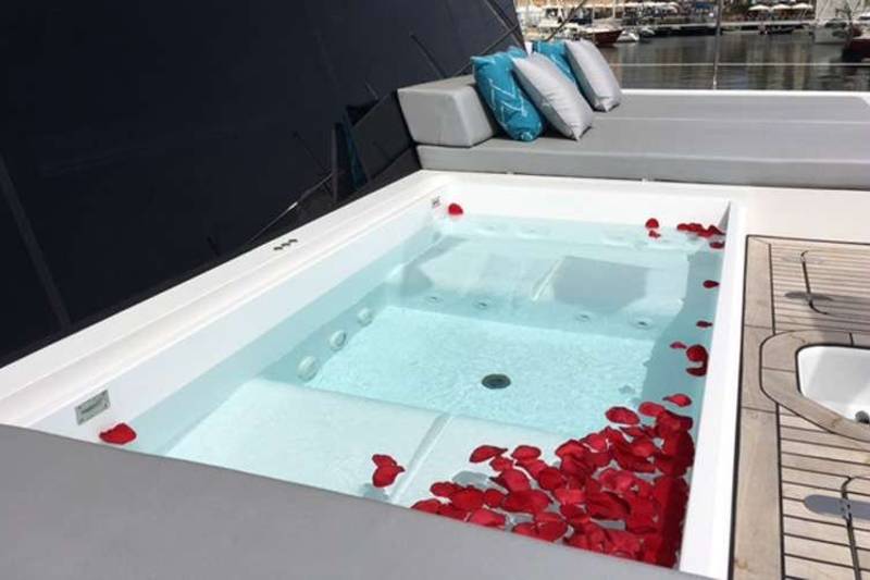 A luxurious yacht jacuzzi is adorned with vibrant red rose petals, inviting a romantic soak at sea.