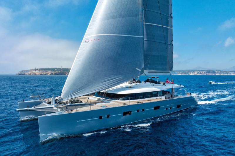 A sleek, modern catamaran glides through the deep blue sea under a vast, cloud-dappled sky.