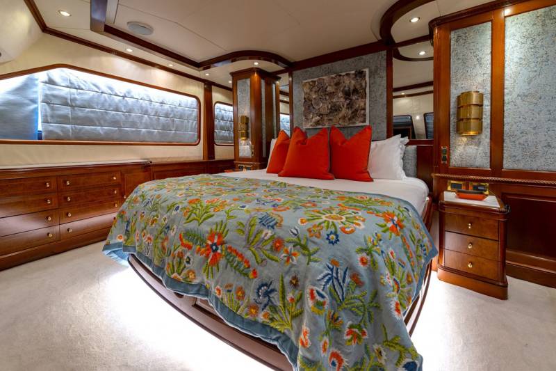 Luxurious yacht stateroom features a vibrant floral quilt on a king-sized bed with elegant wood accents.