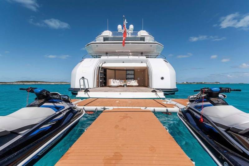 Two jet skis await adventure on the turquoise waters beside a luxurious yacht with an open aft deck.