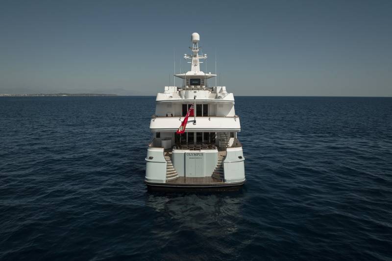 The majestic yacht Olympus glides serenely across the deep blue sea under a clear sky.