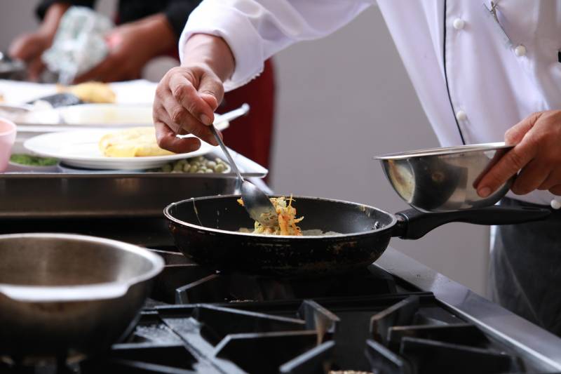 A chef carefully spoons a colorful mixture of vegetables into a hot frying pan.