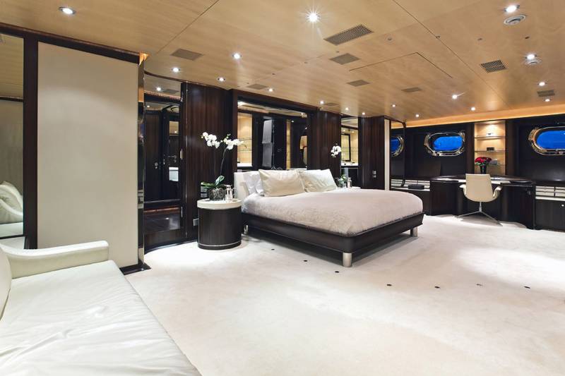 Luxurious yacht stateroom features a plush bed, elegant wood accents, and porthole windows offering a glimpse of the sea.
