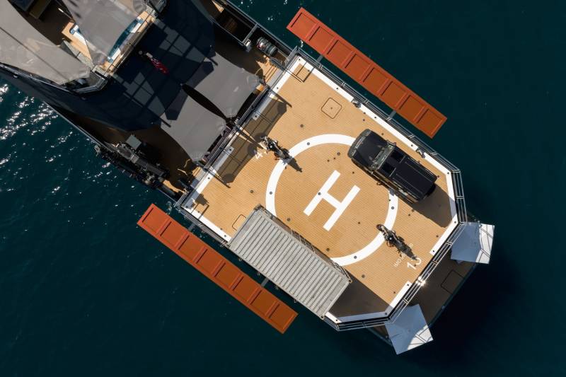 A luxurious yacht with a helipad, car, and motorcycles rests on the calm, dark blue water.