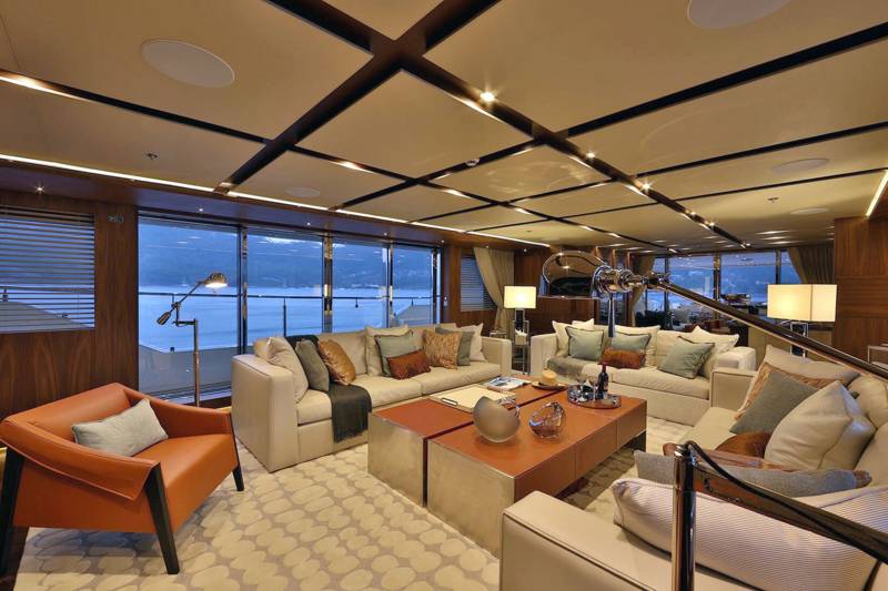 This luxurious yacht salon offers panoramic views of a serene waterfront landscape from its expansive windows.