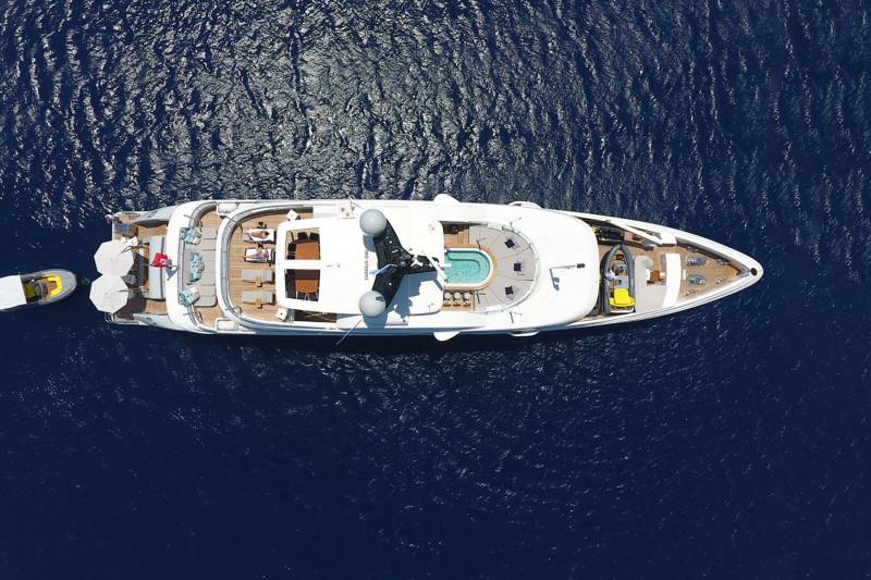 An aerial view captures a luxurious yacht with a pool and tenders floating on the deep blue sea.