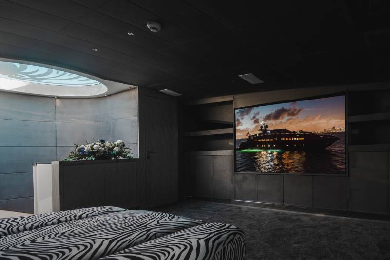 A luxurious yacht is displayed on a large screen in a dimly lit room with zebra-print seating.