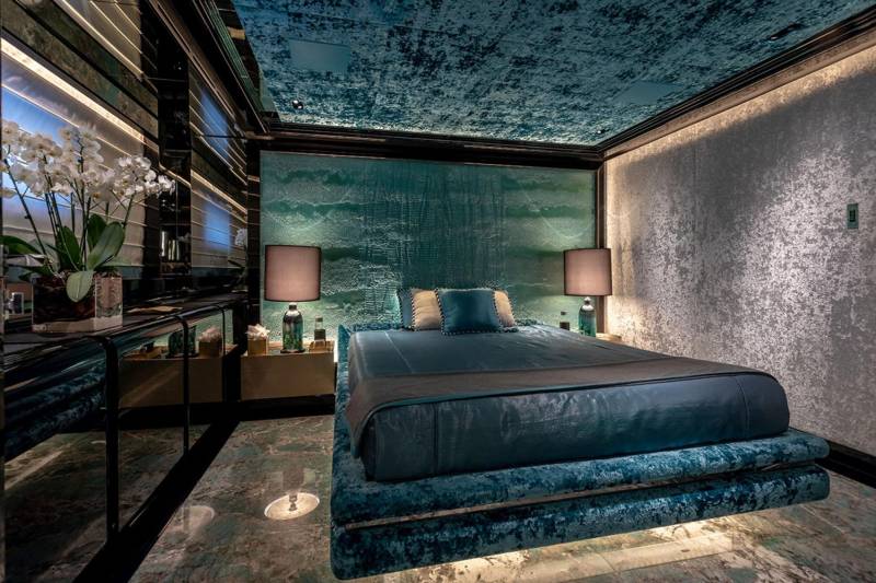 Luxurious bedroom features a plush teal bed, textured teal headboard, and a shimmering, reflective ceiling.