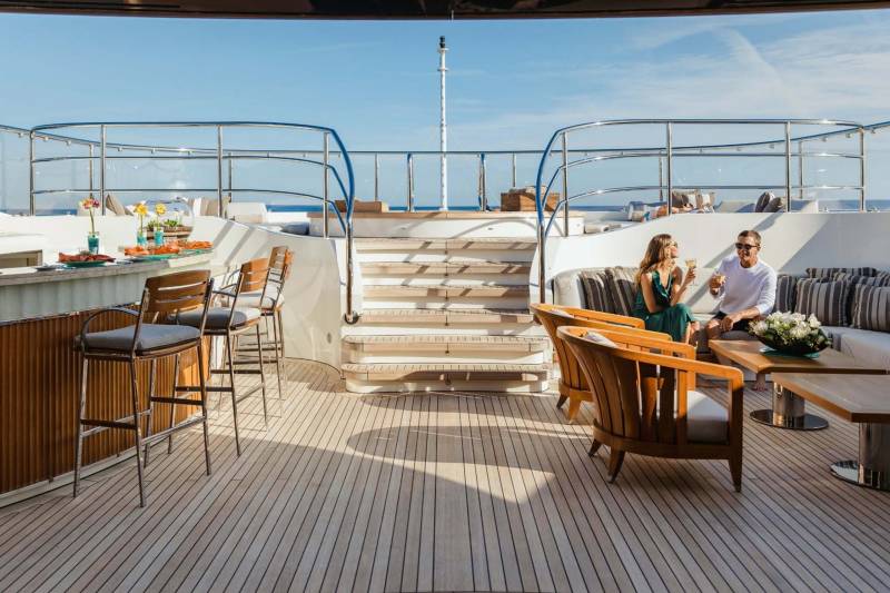 A couple enjoys drinks on a luxurious yacht deck, surrounded by elegant seating and a serene ocean view.