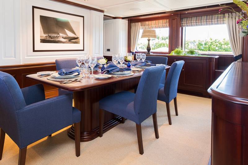 A formal dining table is set with blue napkins and fine china, ready for a meal aboard a luxurious yacht.