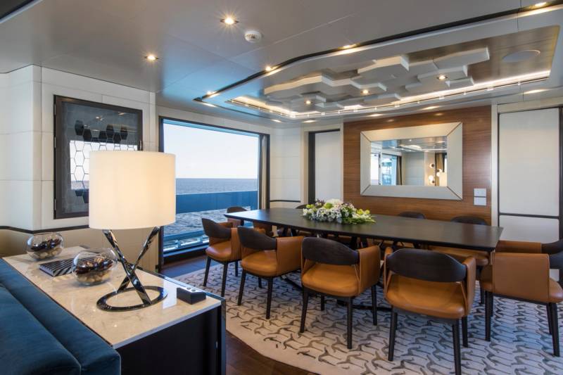 A modern dining area with a large table and comfortable chairs offers stunning ocean views through a panoramic window.