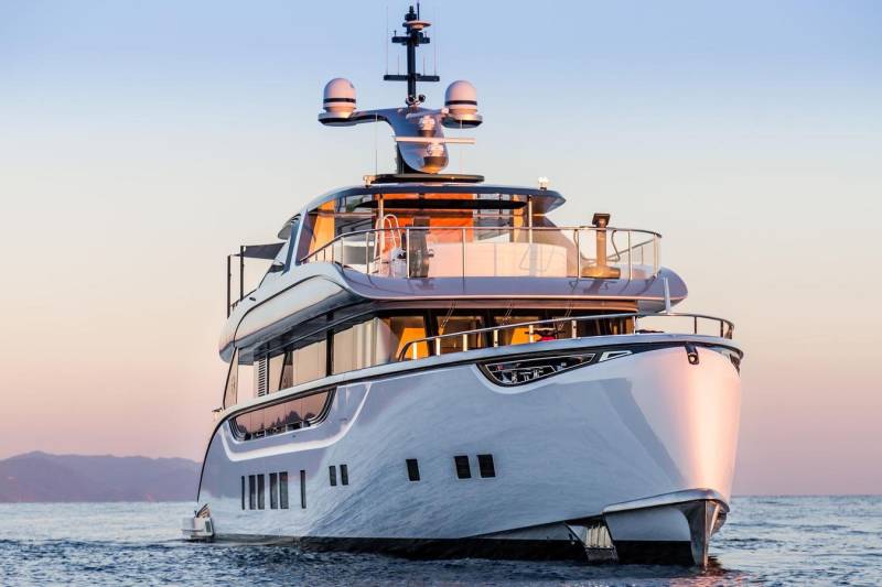 A sleek, modern yacht glides across calm waters at sunset, its elegant lines reflecting the warm hues of the sky.