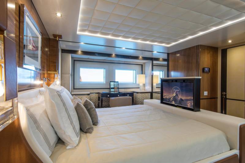 Luxurious yacht cabin features a plush bed, elegant wood paneling, and a hidden television for ultimate comfort.
