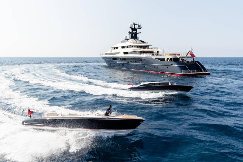 A sleek superyacht cruises the azure sea, flanked by two nimble speedboats cutting through the waves.