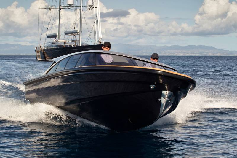 Two men in a sleek black speedboat enjoy a sunny day on the water with a large yacht in the background.