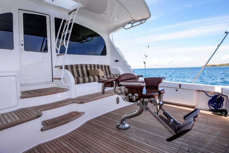 Luxurious teak decks and plush seating invite relaxation on this elegant yacht cruising the azure waters under a bright blue sky.
