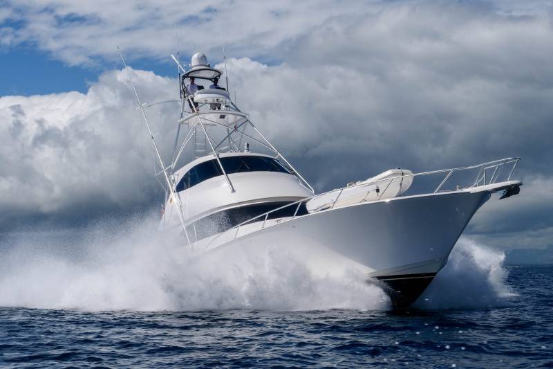 A powerful white yacht cuts through the choppy blue sea, creating a dramatic spray under a cloudy sky.