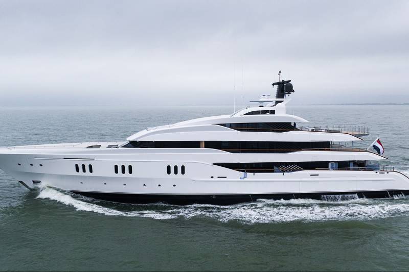 A sleek white superyacht glides through choppy grey waters under an overcast sky.