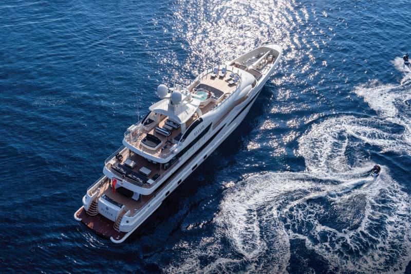 Two jet skiers create foamy trails in the deep blue sea as a luxurious yacht sails nearby.