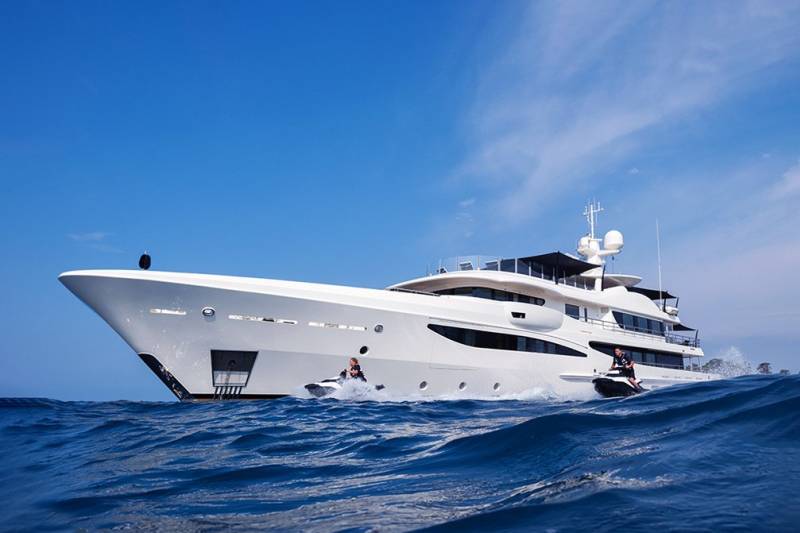A luxurious white yacht cruises through the ocean with two jet skiers enjoying the ride alongside.