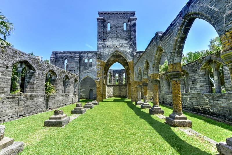 Ancient stone ruins stand against a bright blue sky, with lush green grass carpeting the interior.