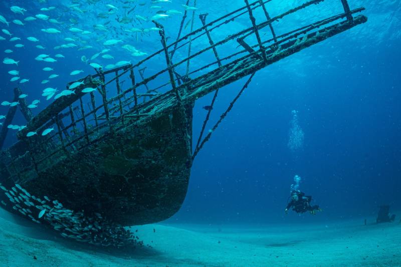 A diver explores a sunken shipwreck teeming with a school of fish in the deep blue ocean.